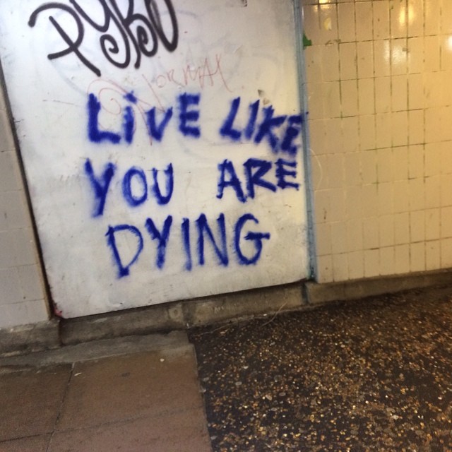 LIVE LIKE YOU ARE DYING blue spray captured in transit in grubby off-white subway