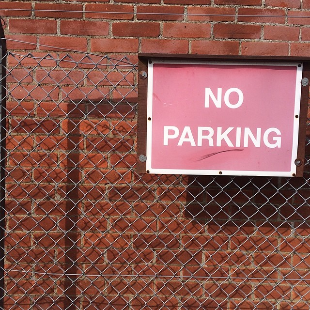 NO PARKING sign on chain link fence, reinforcing red brick wall