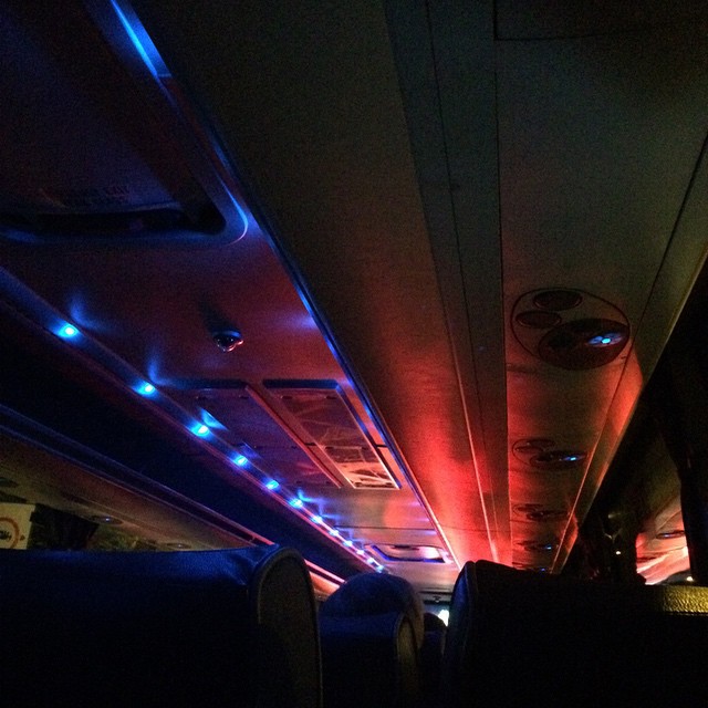 red light washes over coach ceiling punctuated by blue pulses down the aisle