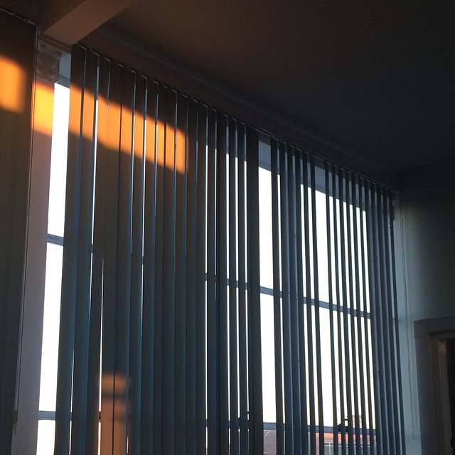 slatted blinds over panes of glass, orange rectangular sunlight intrudes from top left
