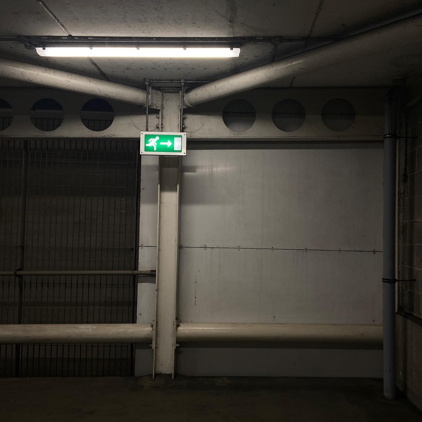 lonely fire exit sign drips from the ceiling, all metal poles and white walls. dark outside