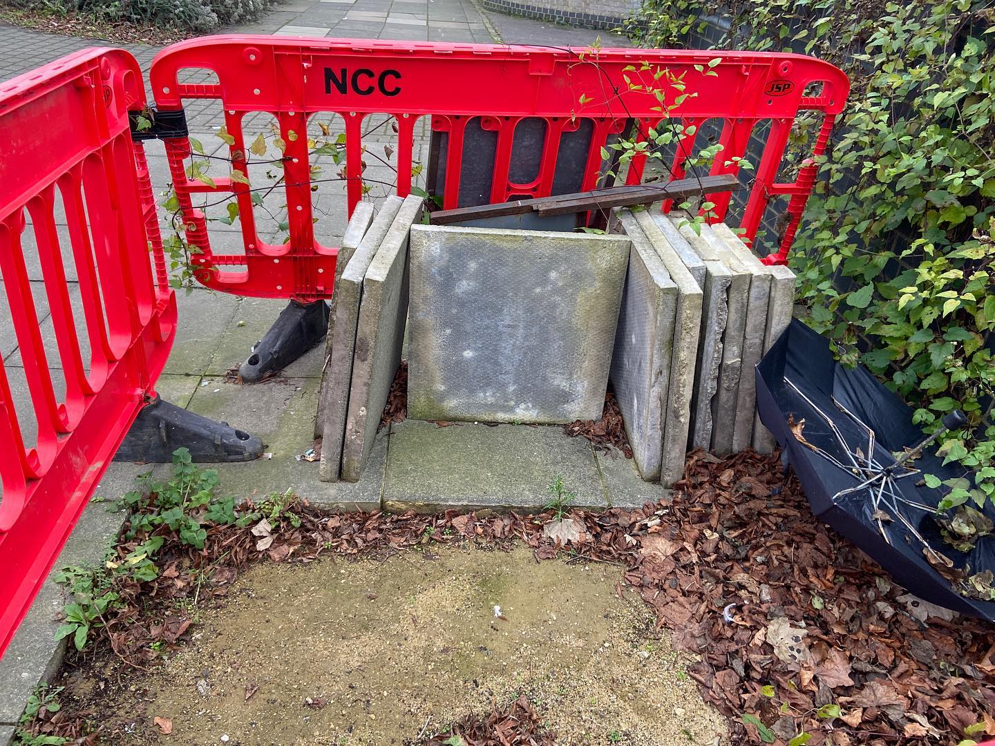 stacked paving slabs watch over the hole they covered, discarded umbrella like dead spider. red NCC barrier segregates