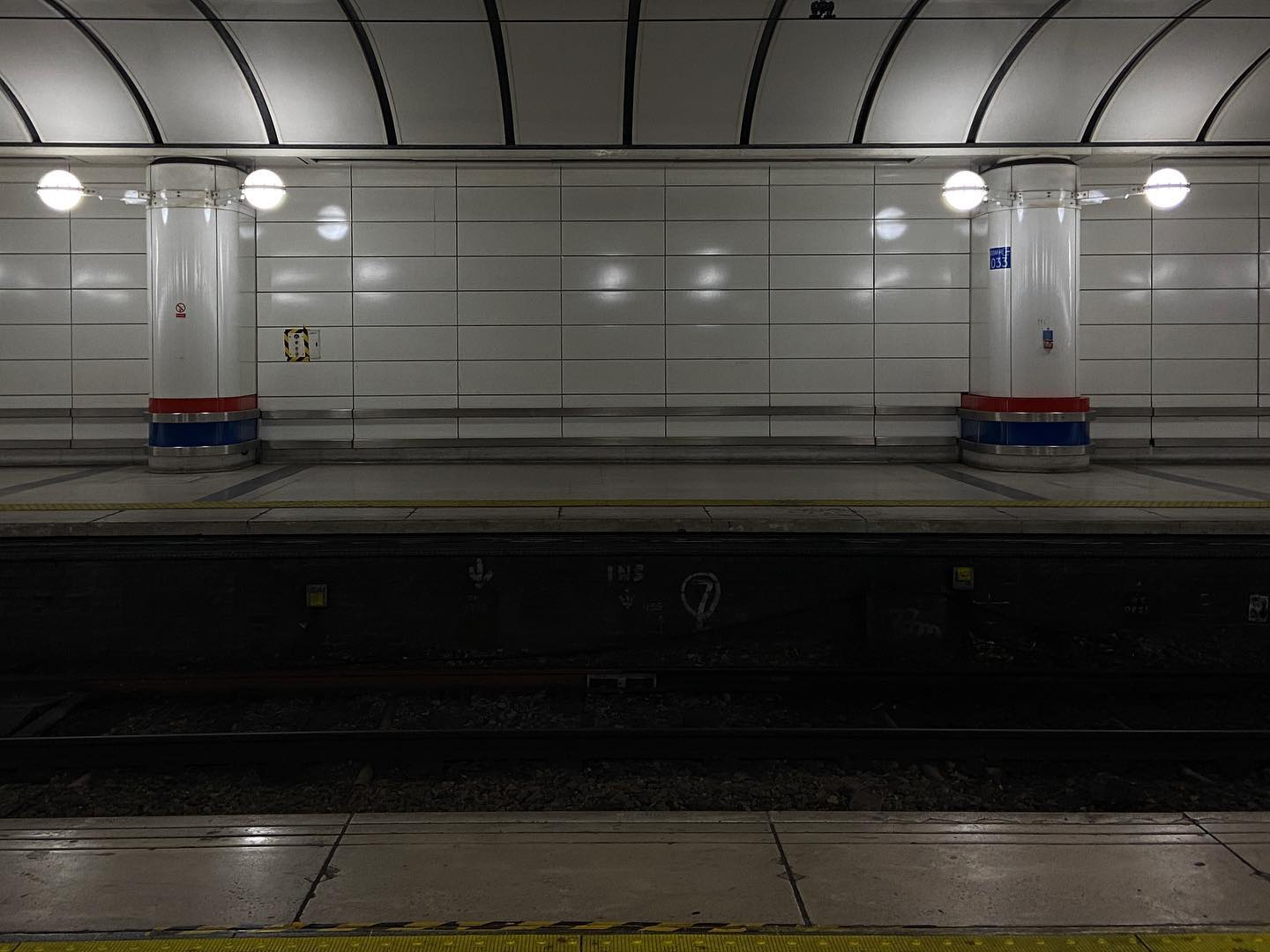 empty platform with globe lights, curving ceiling and parallel tiles. reflections abound in the gloom