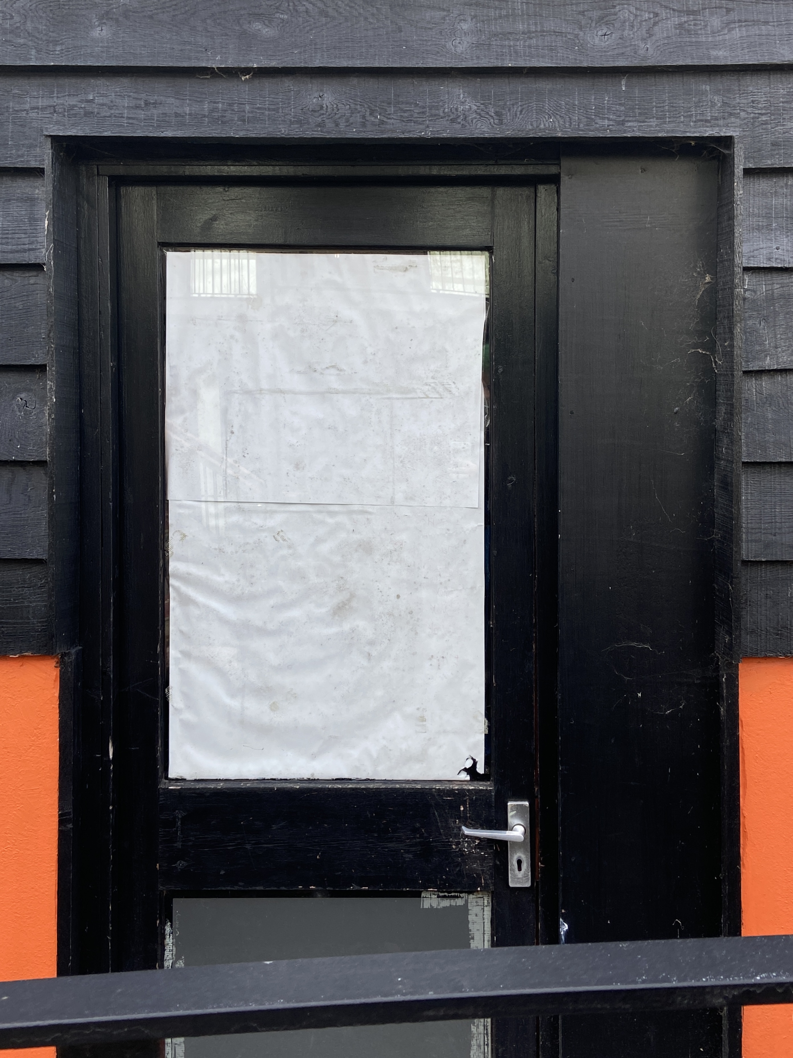whited out window in black framed door, crinkled paper. black panelling over shocking orange