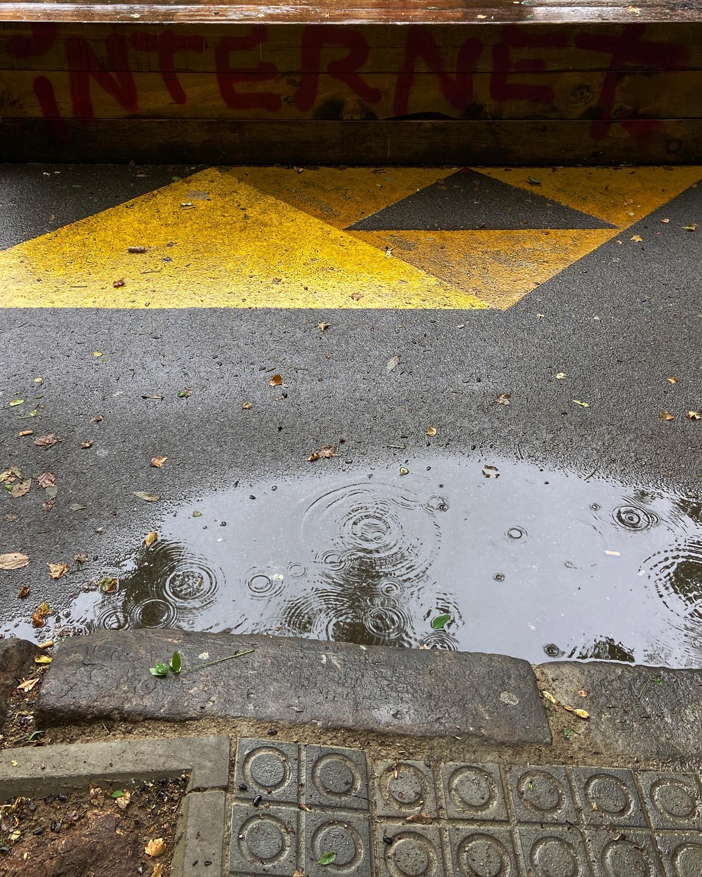 a kerb in the rain, falling. red sprayed INTERNET to the rear, yellow triangles on the ground