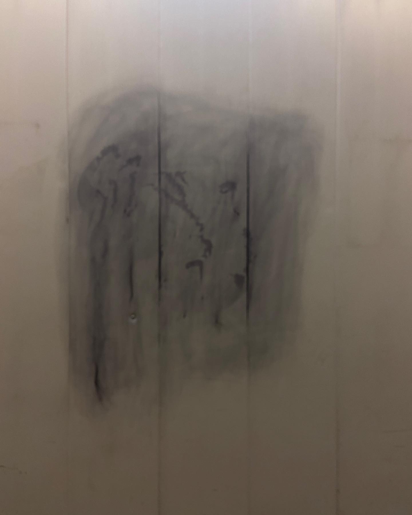 cloudy rubbed out graffiti on white plastic board with vertical joins. the rubbed out graffiti was in black and is darker in the joins of the plastic