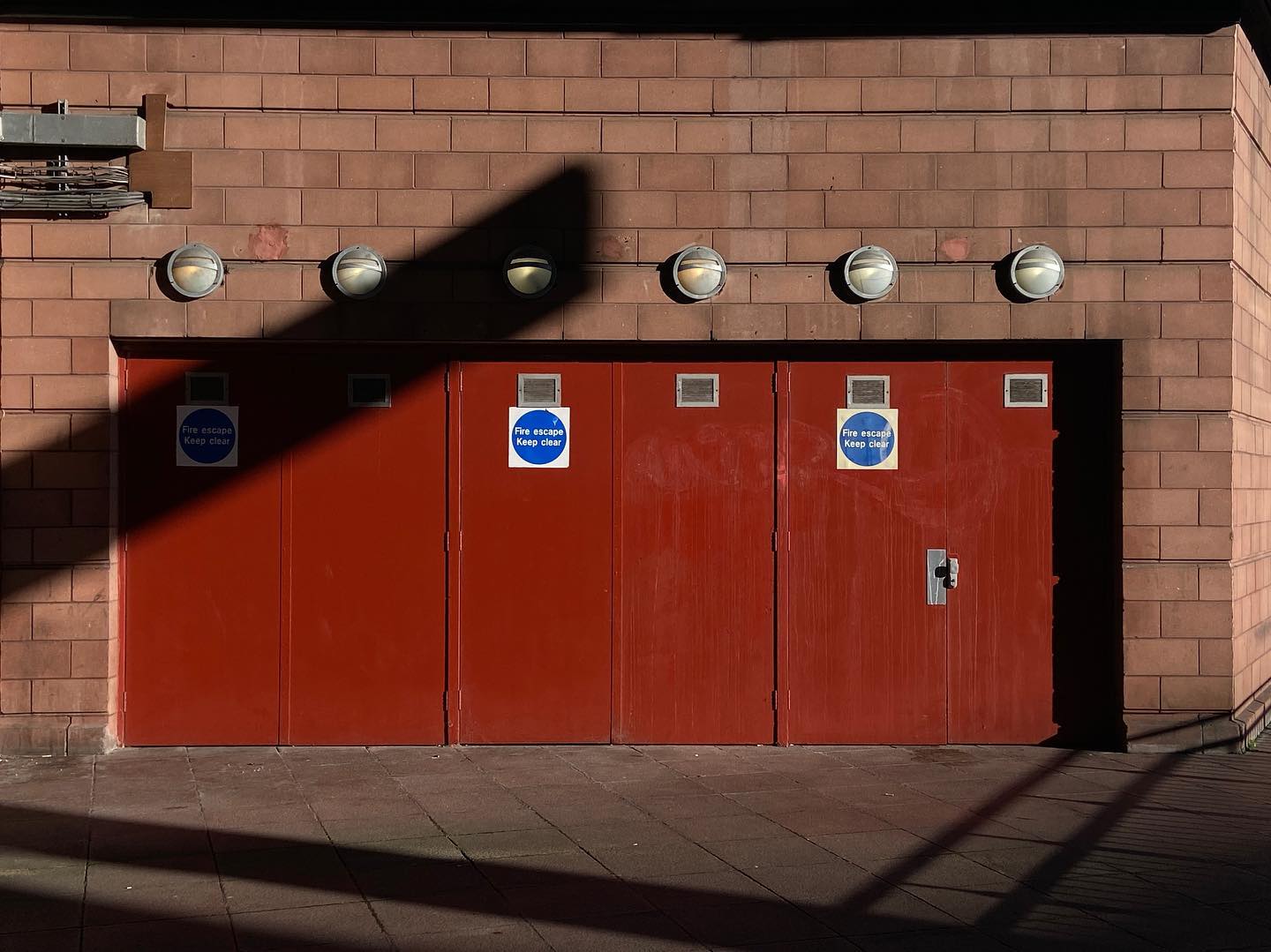 three red doors in a pink brick wall, corresponding round lights adorning. cutting shadow, blue warning signs