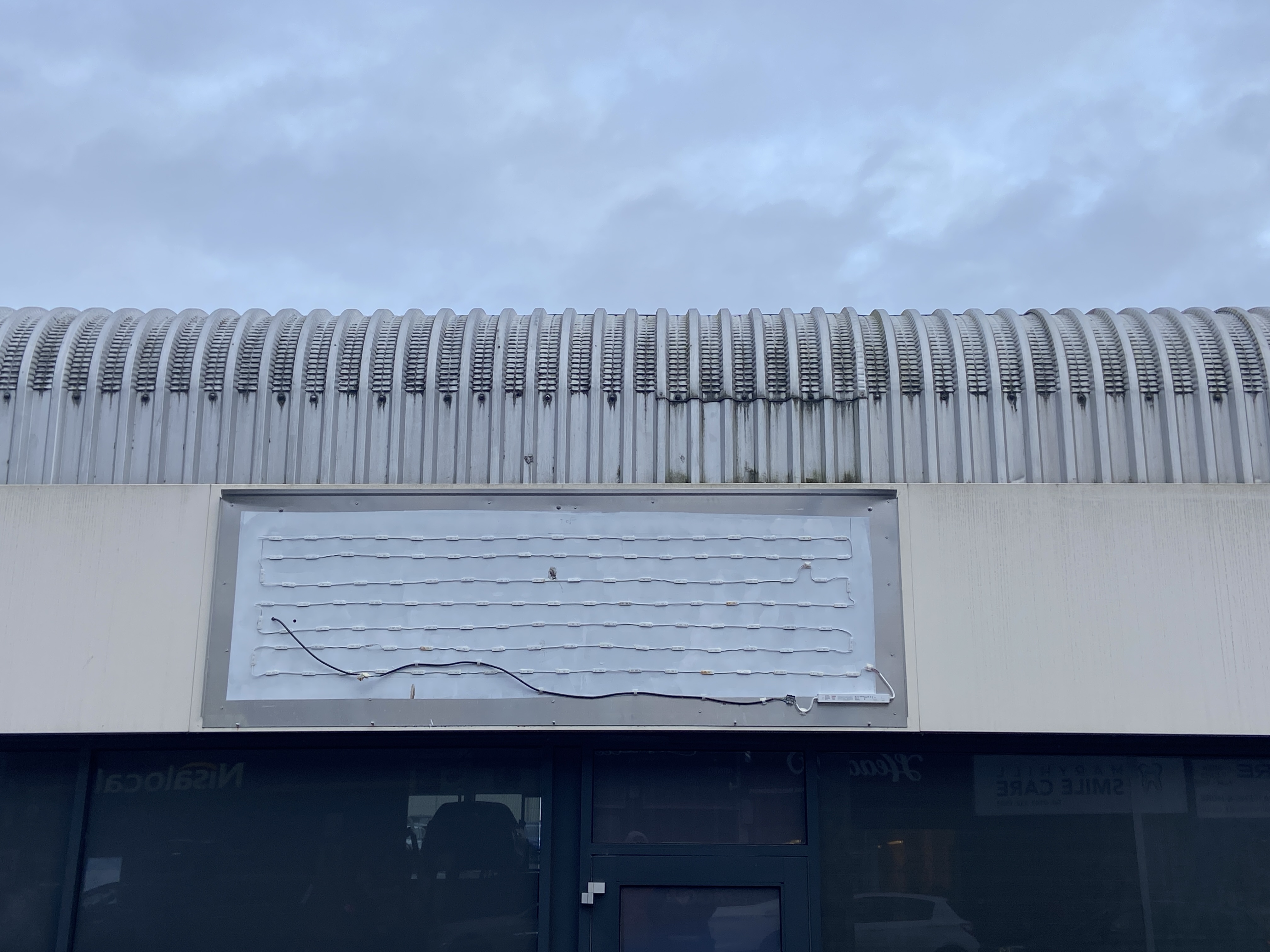 ribbed rounded roof edge against overcast sky. exposed LED impotent signage over dark frontage